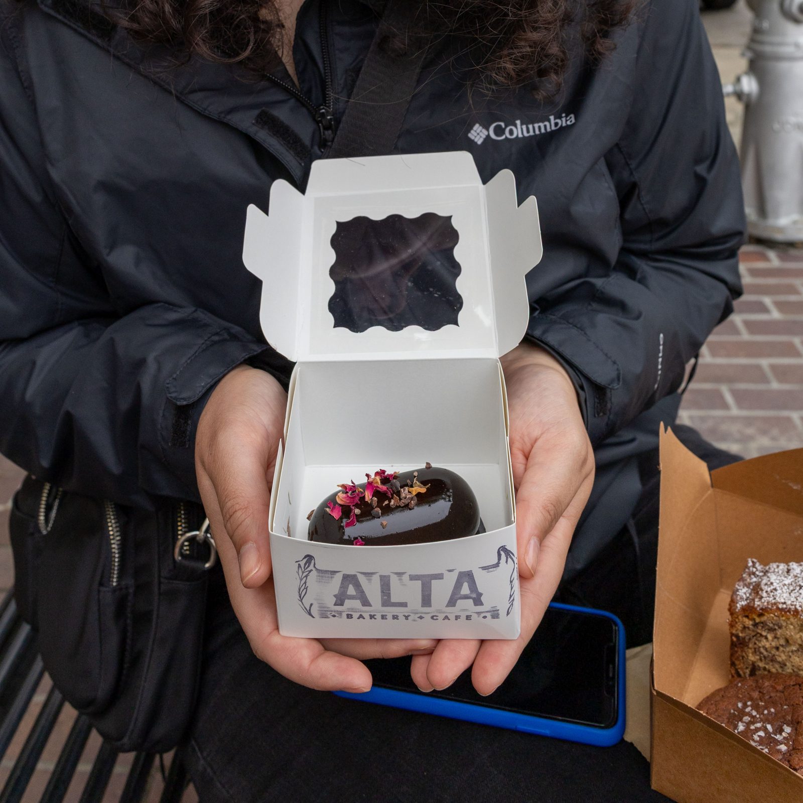 Hands holding a chocolate pastry in an Alta Bakery box in downtown Monterey