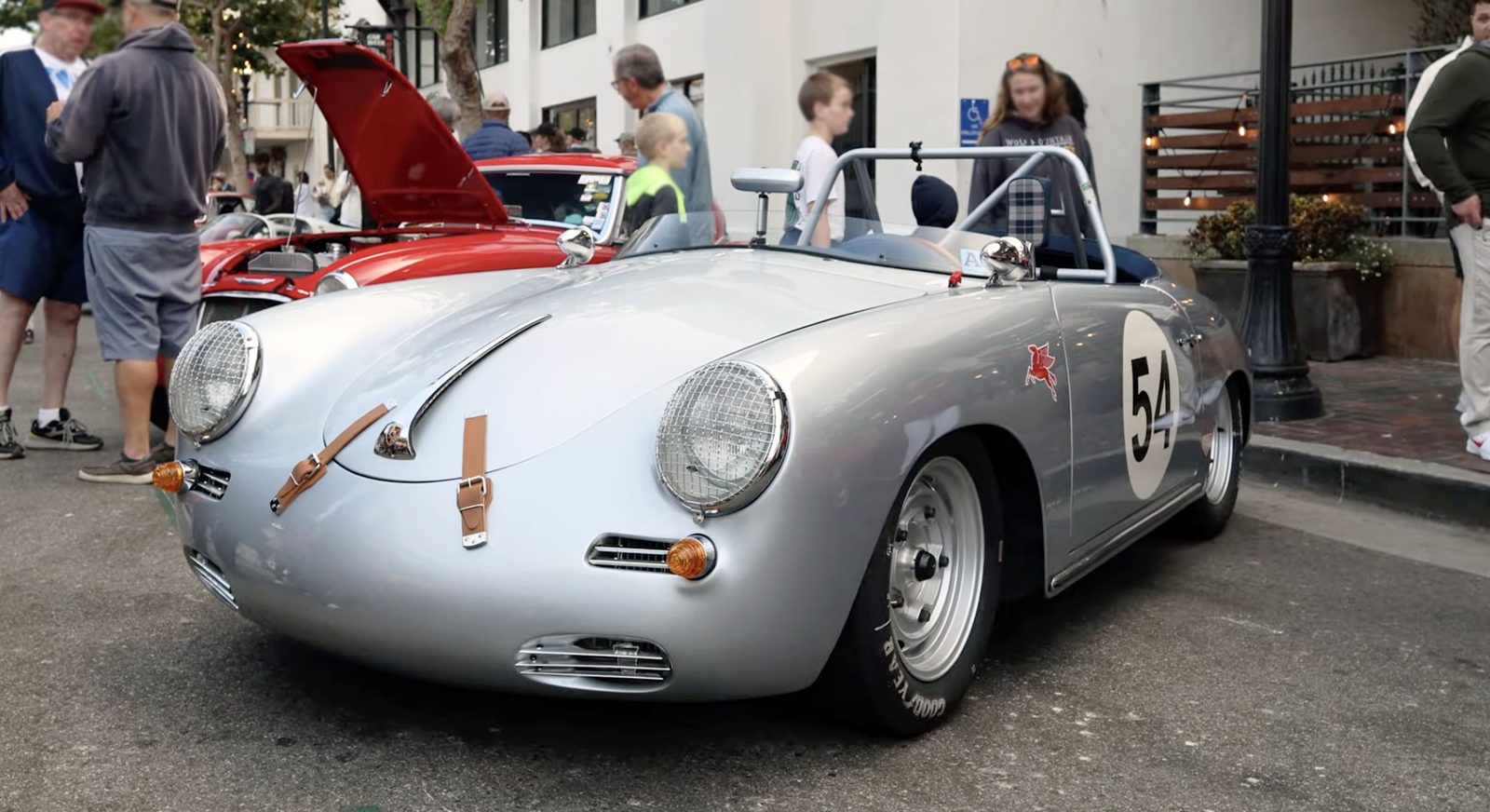 A silver Porsche 356 Speedster with its hood open draws a crowd on the street at the downtown Monterey Car Week kickoff