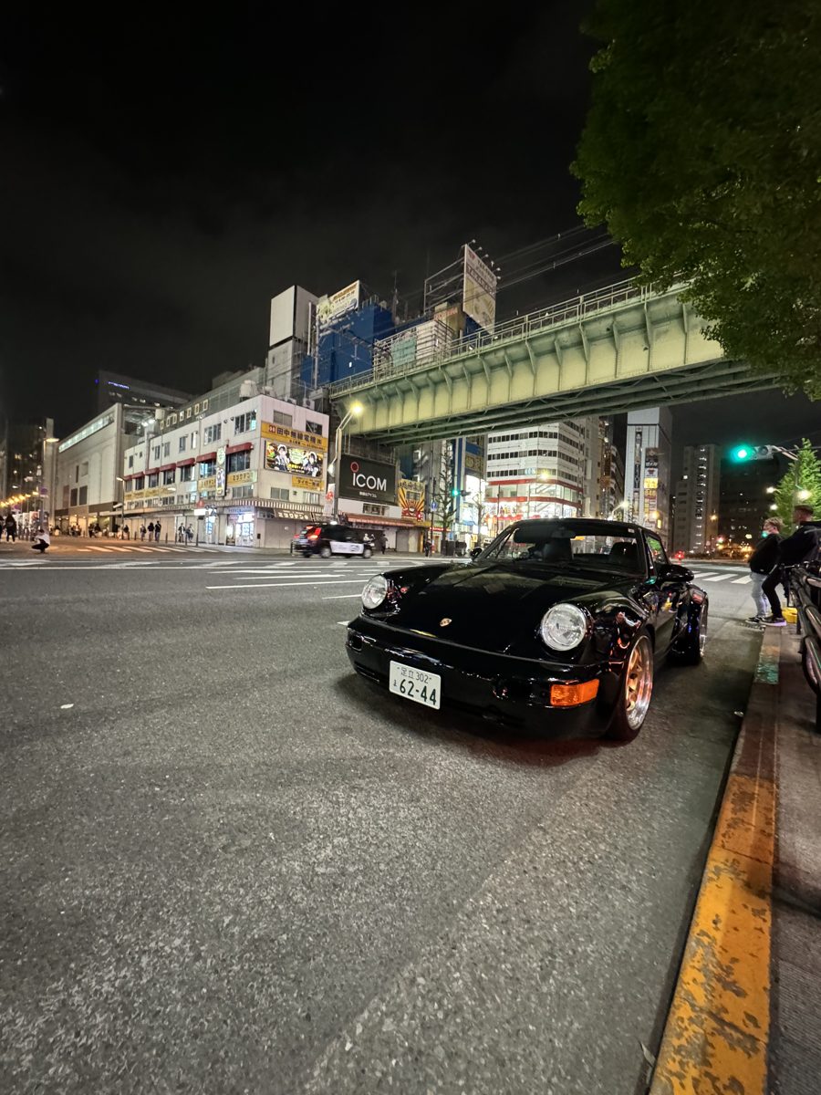 Wide-body black Porsche 911 (964) parked under the Akihabara elevated train tracks