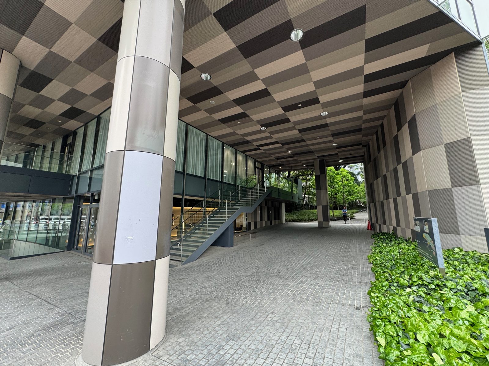 A modern covered plaza in Tokyo with a checkerboard ceiling, staircase, and greenery