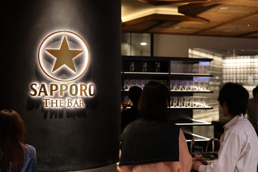 The Sapporo The Bar tasting room with its illuminated gold star logo and rows of glasses