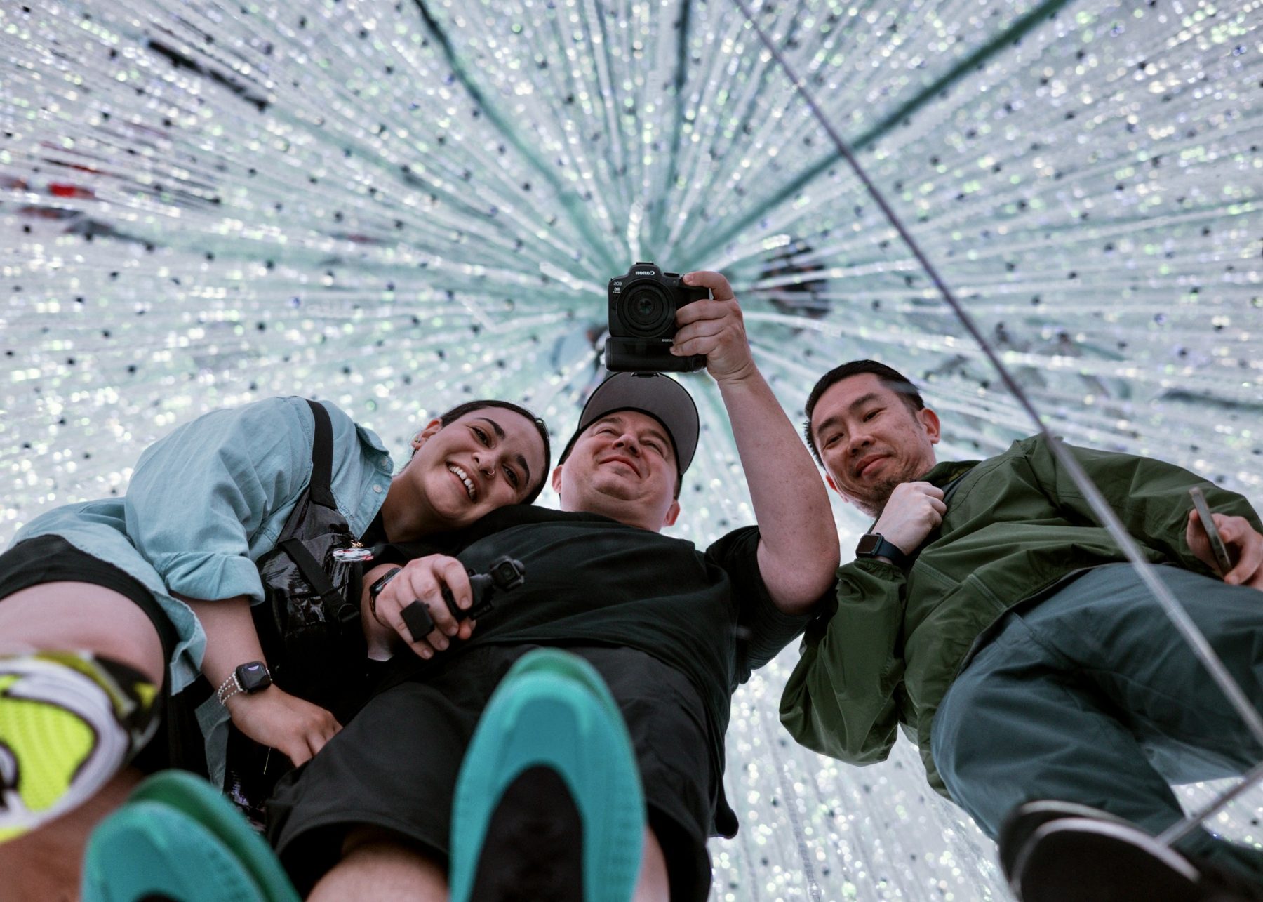 Three friends lying under the teamLab crystal light installation in Tokyo, one holding a camera up